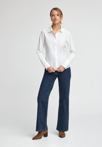White long-sleeve button-up shirt paired with dark blue wide-leg jeans and brown heeled ankle boots. Smooth fabric with a collar.