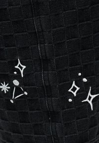 Μαύρο υφασμάτινο ύφασμα με υφή και μοτίβο ραμμένων τετραγώνων, με λευκά κεντημένα αστέρια και λαμπυρίζουσες μορφές.