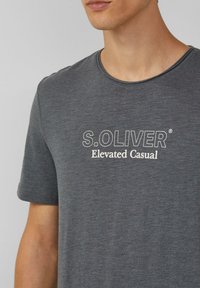 Szary t-shirt z krótkim rękawem z okrągłym dekoltem, z napisem "S.OLIVER Elevated Casual" nadrukowanym na przodzie w białym kolorze. Miękka tekstura.