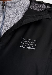 Czarna kurtka z wysokim kołnierzem, szarym wnętrzem i logo Helly Hansen. Materiał jest gładki z teksturowanym siateczkowym detalem.