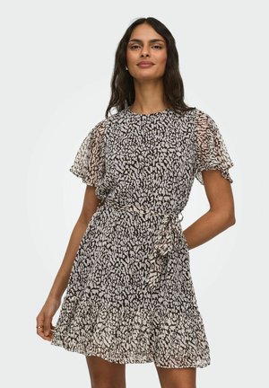 Vrouw poseert in een korte mouwen jurk met ceintuur, zwart-witte dierenprint en gerimpelde zoom, tegen een effen lichte achtergrond.