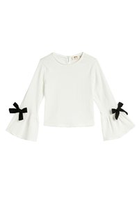 White long-sleeve top with flared sleeves, featuring black bow accents at cuffs and a textured fabric. Round neckline with a back button closure.