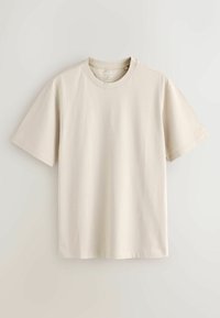 T-shirt beige à manches courtes, coupe décontractée, avec un col rond et une texture de tissu lisse agrémentée de détails de couture subtils.