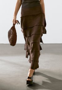 Gonna marrone a strati con orlo ondulato, abbinata a una borsa marrone texturizzata e scarpe platform nere spesse. Un semplice top in maglia completa il look.