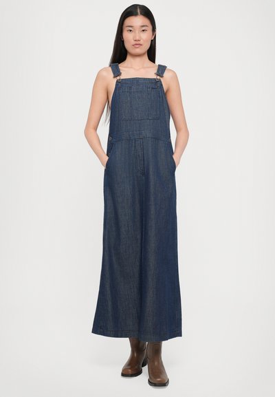 Salopetă din denim de culoare bleu închis, cu bretele ajustabile, buzunare frontale, picioare late și o croială lejeră. Textură solidă cu detalii minime.
