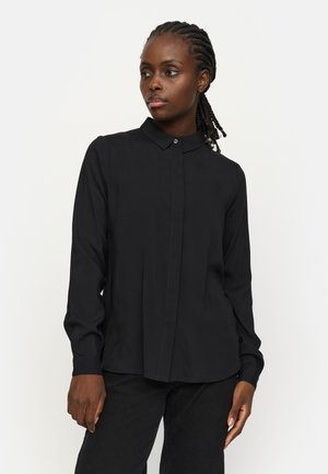 Black long-sleeve shirt with a button-down collar, front pleat detail, and subtle stitching. Soft fabric with a smooth texture, worn with dark pants.