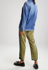 Džínová bunda světle modré barvy, volný střih, s dlouhými rukávy; olivově zelené kalhoty s černými pruhy po stranách; černé baleríny.