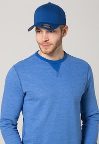Cappellino da baseball blu e maglietta a maniche lunghe blu, entrambi in un morbido tessuto, con colletto a girocollo e dettagli di cucitura a contrasto.