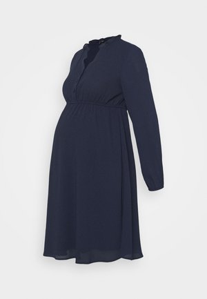 Jūras spēku grūtnieču kleita ar garām piedurknēm, pogu aizdari un volānu apkakli; piedāvā impērijas vidukli, kas nodrošina brīvu piegriezumu. Viegls audums.