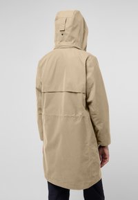 Giacca impermeabile beige con cappuccio, dotata di una patta posteriore, maniche lunghe e taglio dritto. Tessuto liscio e design minimalista.