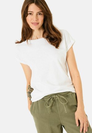 White cotton t-shirt with rolled short sleeves, paired with olive green elastic waist pants featuring a drawstring. Minimalist design.