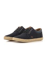 Zapatos de lona negros con acentos de cuero marrón, cordones redondos y suelas similares al yute. Diseño bajo con parte superior transpirable y superficie plana y texturizada.