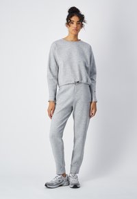 Felpa grigia in cotone e pantaloni jogger coordinati, con vita e polsini con coulisse. Le scarpe sono grigie con accenti bianchi e neri.