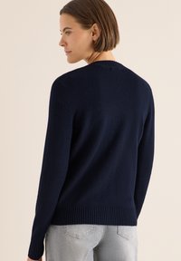 Námořnický modrý pletený svetr s kulatým výstřihem, ribkovaným lemem a manžetami. Měkká struktura a jednoduchý design bez vzorů nebo akcentů.
