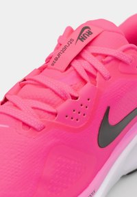 Helles, pinkes Sport Schuhwerk mit einer strukturierten Oberseite, schwarzem Logo-Accent und passenden Schnürsenkeln, ausgestattet mit einer leichten Sohle, die für Komfort sorgt.