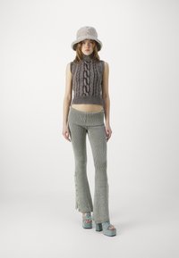 Top de punto sin mangas con diseño de trenzas, combinado con pantalones acampanados de canalé en verde claro. Accesorios incluyen un sombrero de cubo beige y suave y zapatos de plataforma azules.