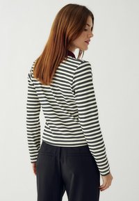 Bluză cu mânecă lungă dungi în crem cu dungi orizontale negre, având un design ajustat și un decolteu rotund, asortată cu pantaloni negri.