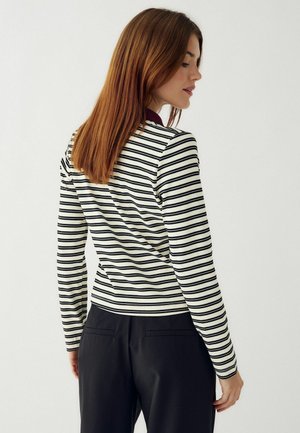 Prúžkované tričko s dlhým rukávom v krémovej farbe s čiernymi vodorovnými pruhmi, s priliehavým strihom a okrúhlym výstrihom, v kombinácii s čiernymi nohavicami.