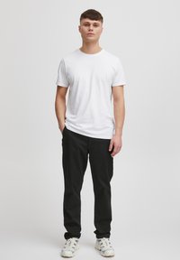 White cotton t-shirt paired with black pants, standing person with short hair. Footwear features a textured design in white and blue.