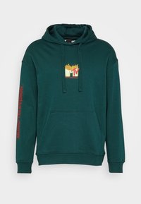 Sweat à capuche vert en tissu doux avec une poche kangourou à l'avant. Graphismes remarquables comprenant le logo "MTV" avec des frites et "MUSIC TELEVISION" en rouge sur la manche.
