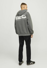 Gray sweatshirt with a hood, featuring white text on the back. Paired with black corduroy pants and dark sneakers with white accents.