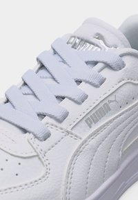 Κοντινή λήψη λευκού αθλητικού παπουτσιού Puma με υφασμένα κορδόνια, ραφές από δερμάτινα πάνελ και λογότυπο Puma στο πλάι και τη γλώσσα.