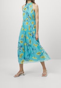 En halterneck, ärmlös klänning i ljusblått med gula blommönster, som har en åtsittande midja och en flödande kjol som når anklarna.