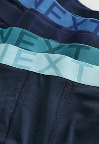 Štyri páry tmavomodrých boxeriek s elastickými pásmi v odtieňoch modrej, z ktorých každé má veľké písmená slov "NEXT".