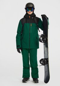 Grøn snowboardjakke og -bukser med sorte accenter, handsker, hjelm og skibriller. Holder en snowboard med sorte bindinger. Teksturerede materialer.
