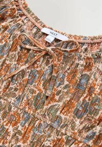 Višebojna cvjetna bluza s ruffles izrezom, s uzorcima narančaste, zelene i plave boje. Zatvara se mašnom sprijeda, izrađena je od mekanog materijala.