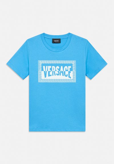 Μπλε κοντομάνικη μπλούζα με λευκό λογότυπο Versace στο κέντρο, περιβαλλόμενο από πλαίσιο με μυκηναϊκό σχέδιο στην μπροστινή πλευρά.