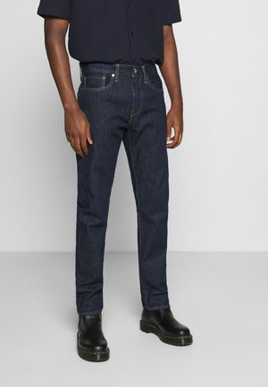 Dunkelblaue Denim-Jeans mit geradem Schnitt, ausgestattet mit gelben Nähten, fünf Taschen und einem Knopfverschluss. Getragen mit schwarzen Stiefeln.
