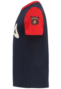 T-shirt di cotone blu navy con maniche rosse, caratterizzato da una stampa di un orso sulla manica sinistra e un grande logo bianco sul davanti. Design corto e aderente.