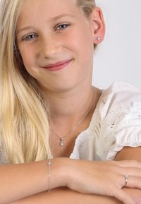 Silberner Schmuck mit floralen Motiven, bestehend aus einer Anhänger-Halskette, einem Armband und einem Ring, jeweils mit einem kleinen Kristall ausgestattet. Strukturierte weiße Bluse.