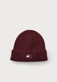 Burgundy knit beanie with ribbed texture, featuring a fold-over cuff and a rectangular logo patch in white and navy.