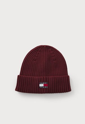 Burgundy knit beanie with ribbed texture, featuring a fold-over cuff and a rectangular logo patch in white and navy.