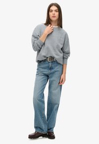 Sudadera gris con cuello redondo, ajuste holgado. Jeans de denim azul, de pierna recta, cintura alta. Botas gruesas marrón oscuro. Diseño simple, sin patrones.