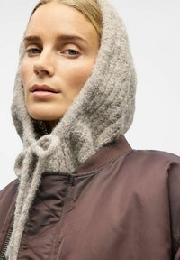Veste aviateur marron avec une capuche en tricot gris clair texturé. La capuche dispose d'une fermeture à nouer à l'avant, ajoutant chaleur et détail.