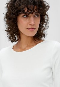 Witte geribbelde lange mouw top met een ronde halslijn. Het materiaal lijkt zacht en lichtjes gestructureerd, dicht op het lichaam aansluitend.