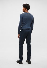 Marinblå ribbad tröja med långa ärmar, kombinerad med marinblå byxor med raka ben och svarta skor, sedd bakifrån mot en ljus bakgrund.