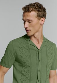 Korte mouwen groene gebreide shirt met een gestructureerd ruitpatroon aan de voorkant, een geknipte kraag en knoopsluiting.