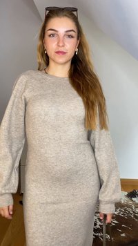 Adīta, gaiši pelēka kleita ar garām pūkainām piedurknēm un noapaļotu dekoltē, kas izceļas ar gludu tekstūru un pieguļošu siluetu.