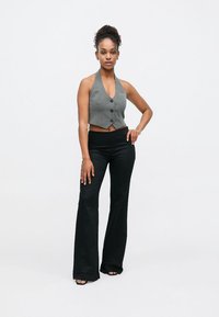 Pelēka cropped veste ar trim pogām, kombinēta ar melnām flares biksēm. Gluda tekstūra, mūsdienīgs dizains un atvērts kakla izgriezums dominē šajā apģērbā.