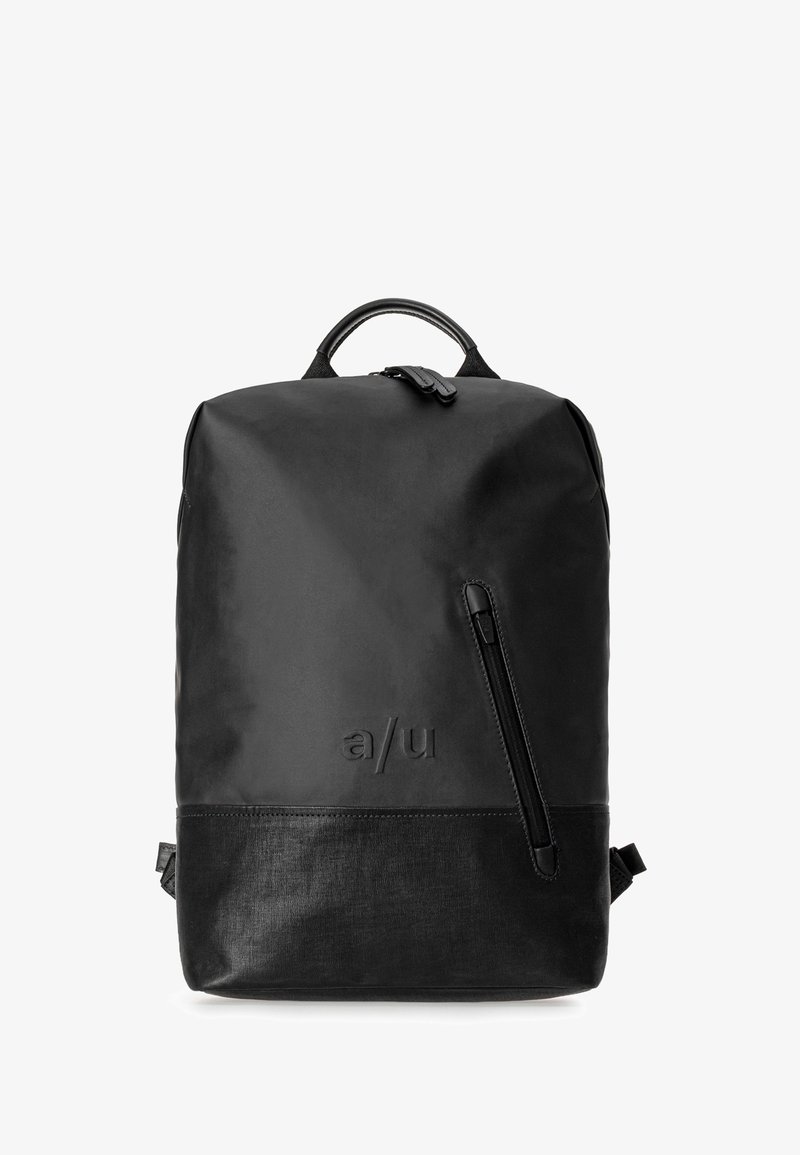 Sac à dos minimaliste noir avec poignée supérieure, poche zippée diagonale à l'avant et logo embossé "a/u" sur matériau supérieur lisse et inférieur texturé.