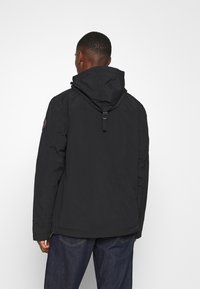 Giacca nera con cappuccio e chiusura con zip, dotata di cappuccio arricciato e cinturini regolabili. Tessuto testurizzato con finitura liscia, dettagli minimi.