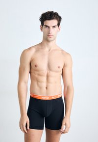 Black Nike boxer briefs with an orange waistband, elastic material, fitted design, and smooth texture, displayed on a male model.