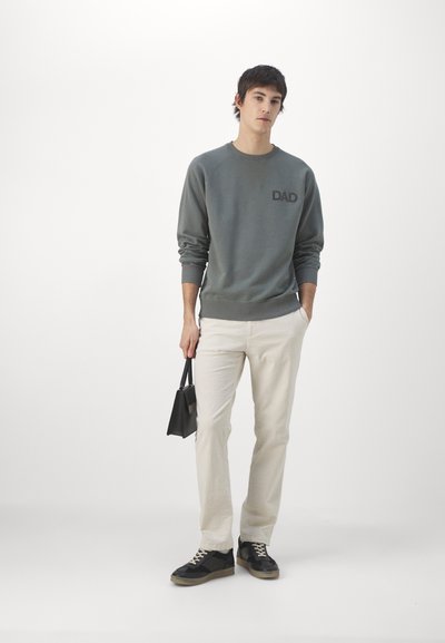 Gray sweatshirt with "DAD" text on the chest, cream-colored pants, black bag, and black sneakers with beige accents.