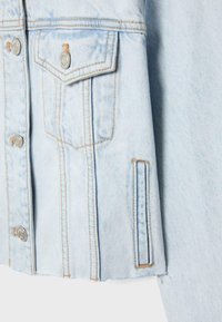 Fragment jasnoniebieskiej kurtki dżinsowej z metalowymi guzikami, kieszenią na piersi z klapką oraz boczną kieszenią z rozcięciem i pomarańczowymi detalami szwów.