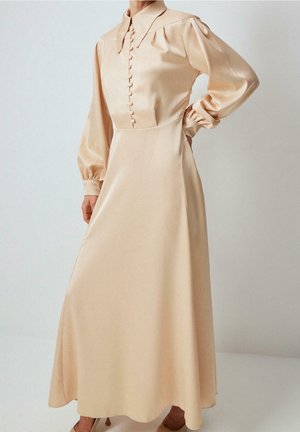 Beżowa satynowa sukienka z długim rękawem, zapinana z przodu na guziki, z marszczonymi mankietami, usztywnionym kołnierzem i dopasowaną talią, która przechodzi w zwiewną spódnicę.
