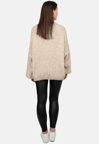 Maglione lavorato a maglia beige con maniche ampie, motivo testurizzato e vestibilità morbida, abbinato a leggings neri lucidi e sneakers bianche.